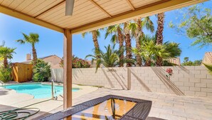 Un espace aménagé au bord de la piscine, avec une table en verre, une pergola en bois et des palmiers.