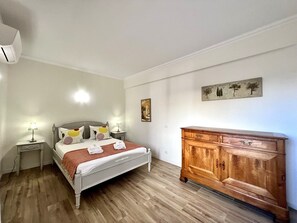 A bedroom with a bed, bedside tables, a wooden dresser, and a wall-mounted artwork.