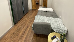 A small, cozy room with two beds, a wooden floor, a small table with a plant, and a painting on the wall. - 
Secluded Mountain Container - Hot Tub & King Bed (Hatfield)