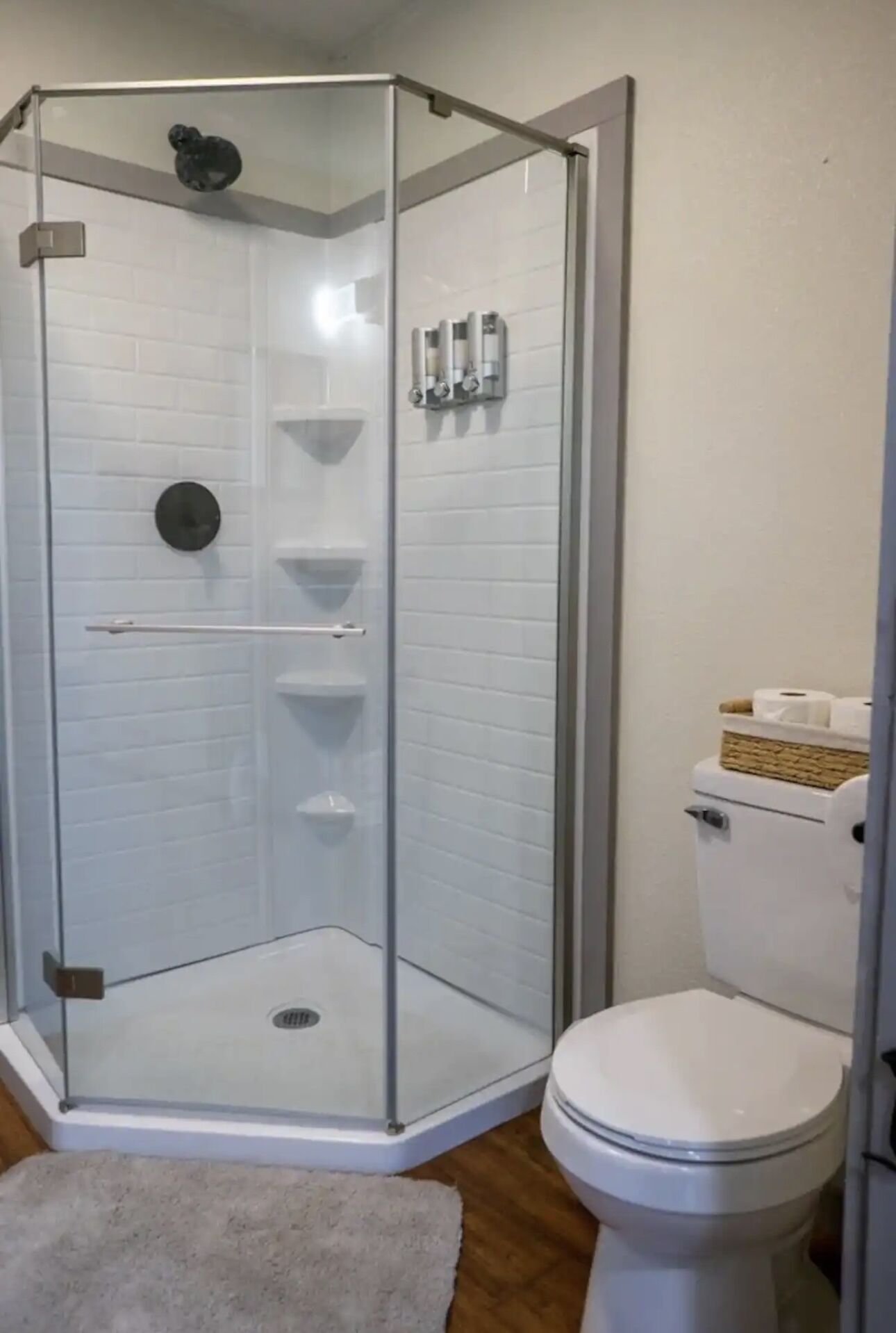 A corner shower enclosure with a glass door, a toilet, and a small rug.