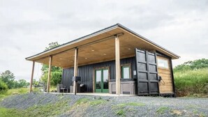 A modern cabin with a covered porch, large windows, and a wooden exterior. - 
Secluded Mountain Container - Hot Tub & King Bed (Hatfield)