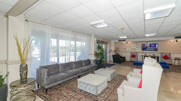 A spacious lobby with a grey sofa, white armchairs, and a patterned rug.