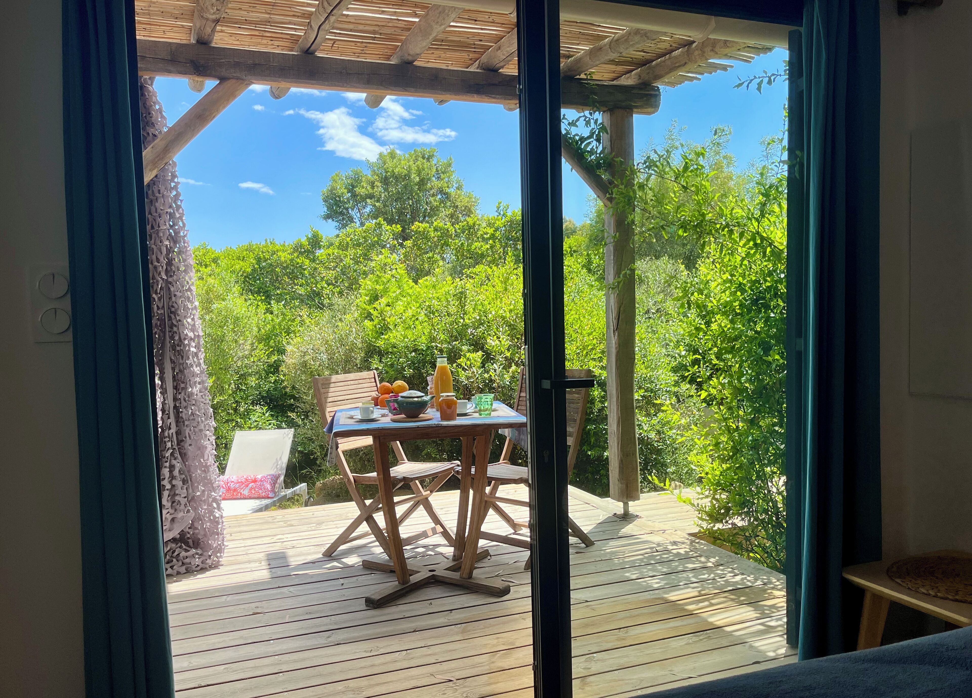 Um deck de madeira com uma mesa posta para o café da manhã, com vista para um jardim exuberante.