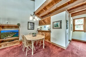A dining area with a wooden table and chairs, a TV on a wooden stand, and a red carpet. - Northstar Resort 2BR 2BA Condo. Forest Views. Pools, Pickleball, Trails & More (Truckee)