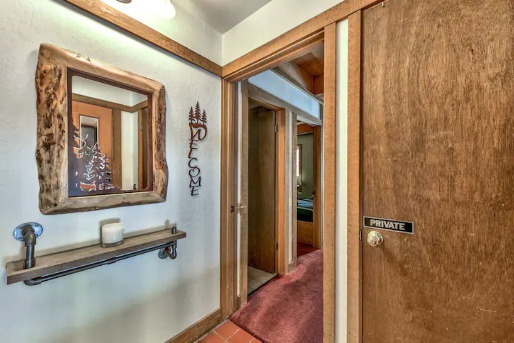 A hallway with a wooden door labeled "PRIVATE," a mirror with a rustic frame, and a shelf with a candle and a small decorative item.