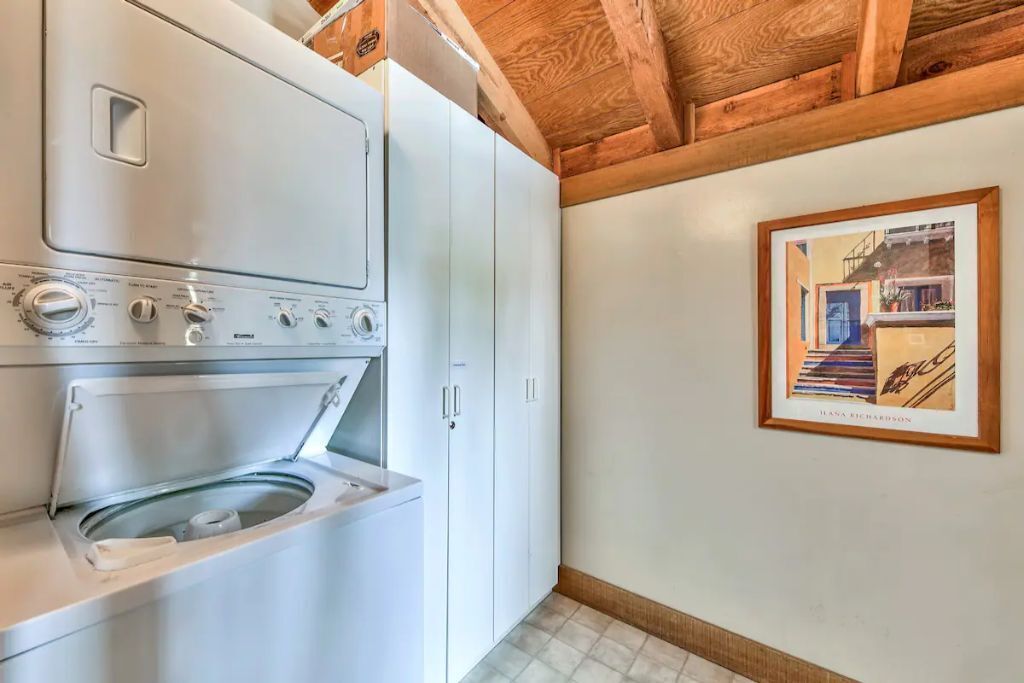 Ein Waschraum mit Waschmaschine und Trockner, Holzbalkendecke und einem gerahmten Bild an der Wand.