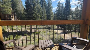 A wooden deck with two lounge chairs and a table, overlooking a forested area with tall trees and a clear sky. - Northstar Tahoe Summer Resort Condo: Pools, Pickleball, Hike Trails, 2BR 2BA (Truckee)