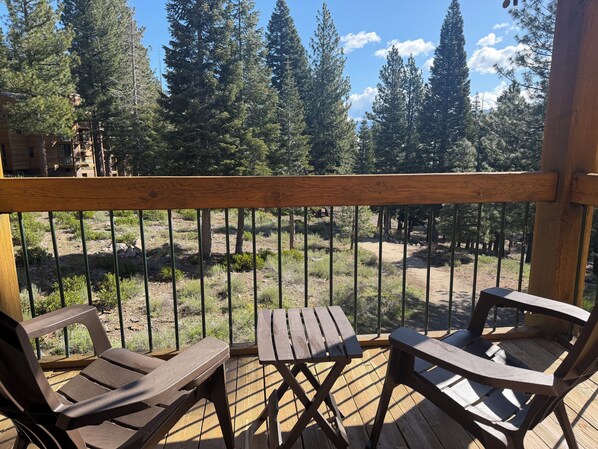A wooden deck with two lounge chairs and a table, overlooking a forested area with tall trees and a clear sky. - Northstar Tahoe Summer Resort Condo: Pools, Pickleball, Hike Trails, 2BR 2BA (Truckee)