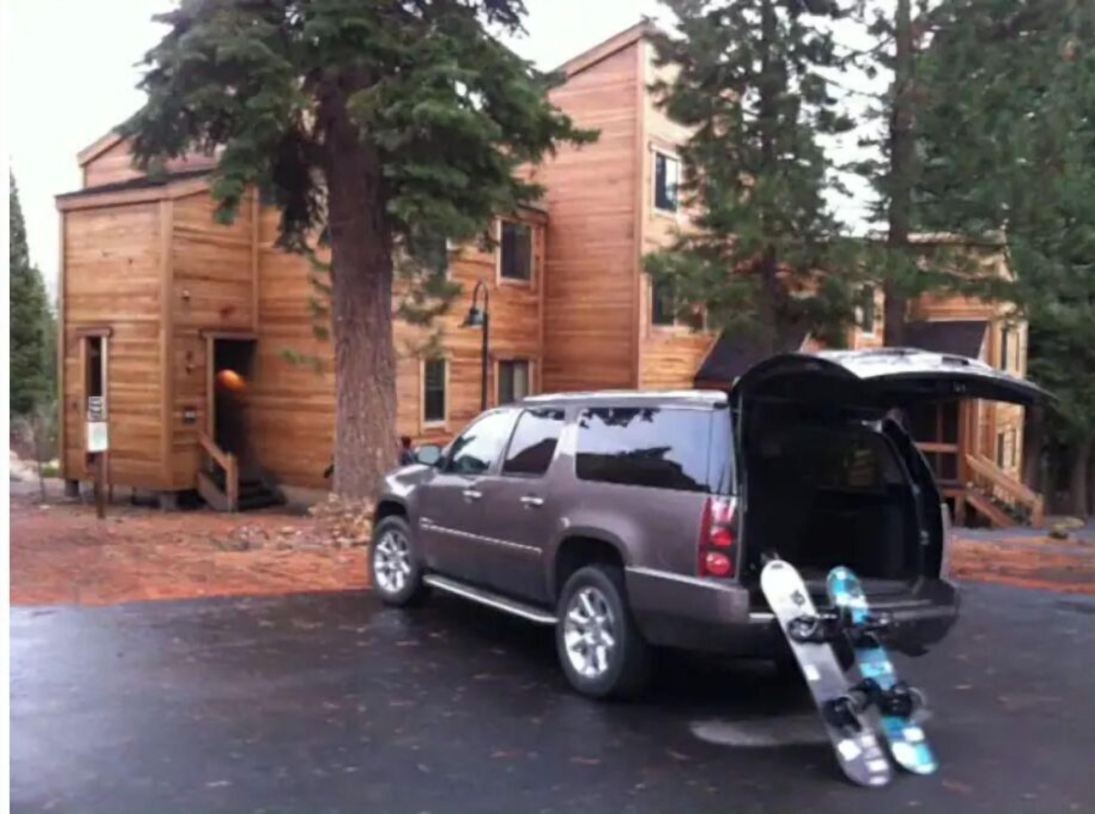 Una cabaña de madera con un coche estacionado adelante y una tabla de snowboard apoyada en el vehículo.