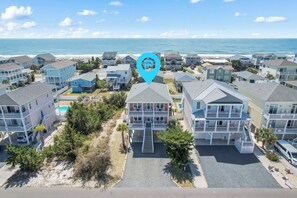 Un quartier résidentiel en bord de mer, composé de plusieurs maisons à deux étages, d’une piscine et d’une plage en arrière-plan.