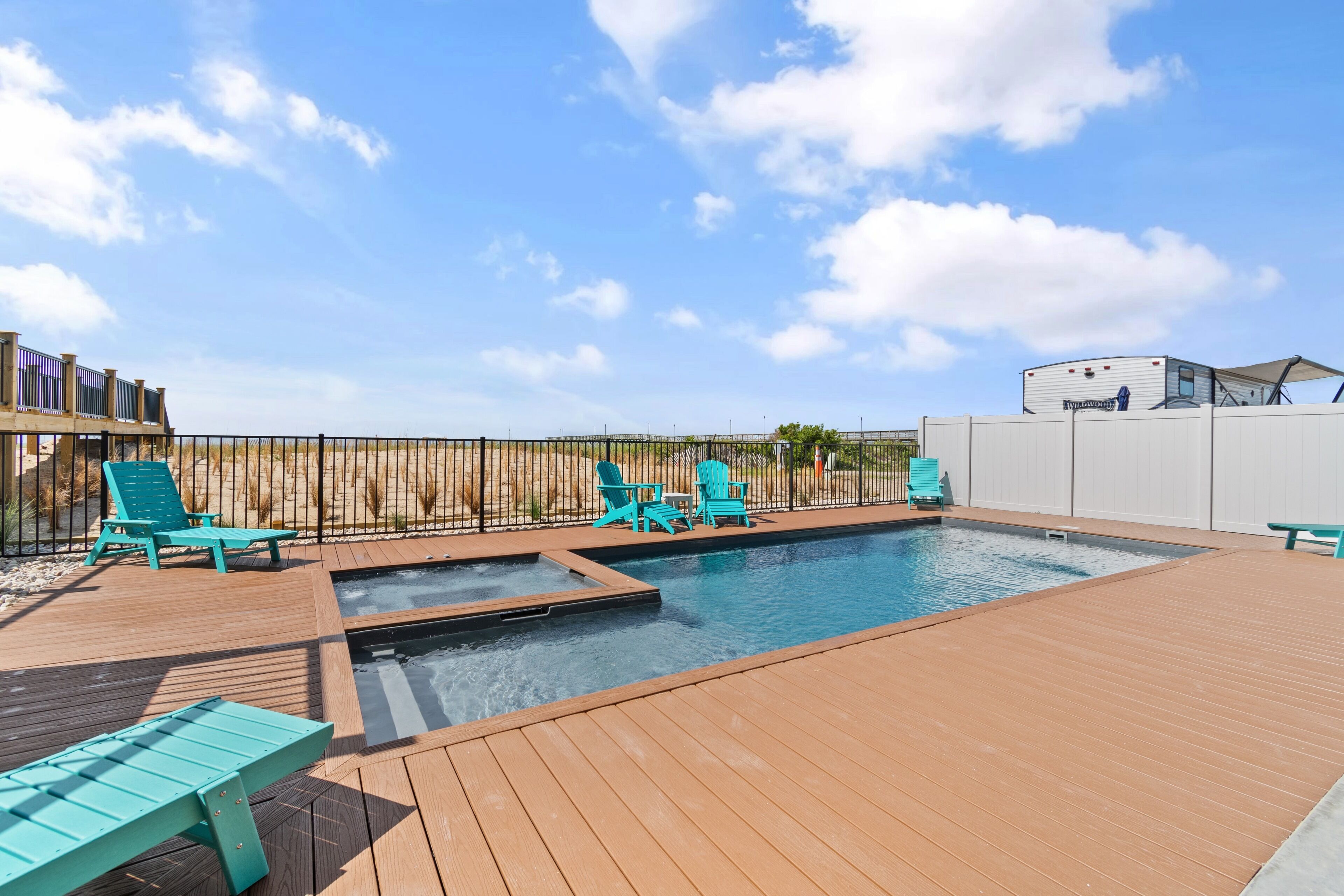 A swimming pool with a wooden deck, surrounded by turquoise lounge chairs and a white fence.