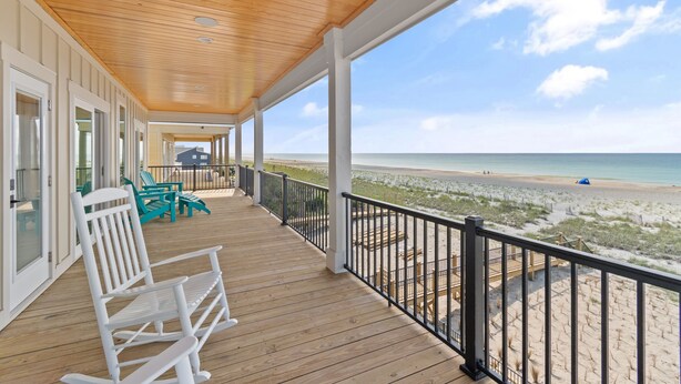 A wooden deck with white rocking chairs and a view of the beach.