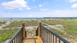 A wooden boardwalk leading to a beach with a wooden fence and a pier in the background.