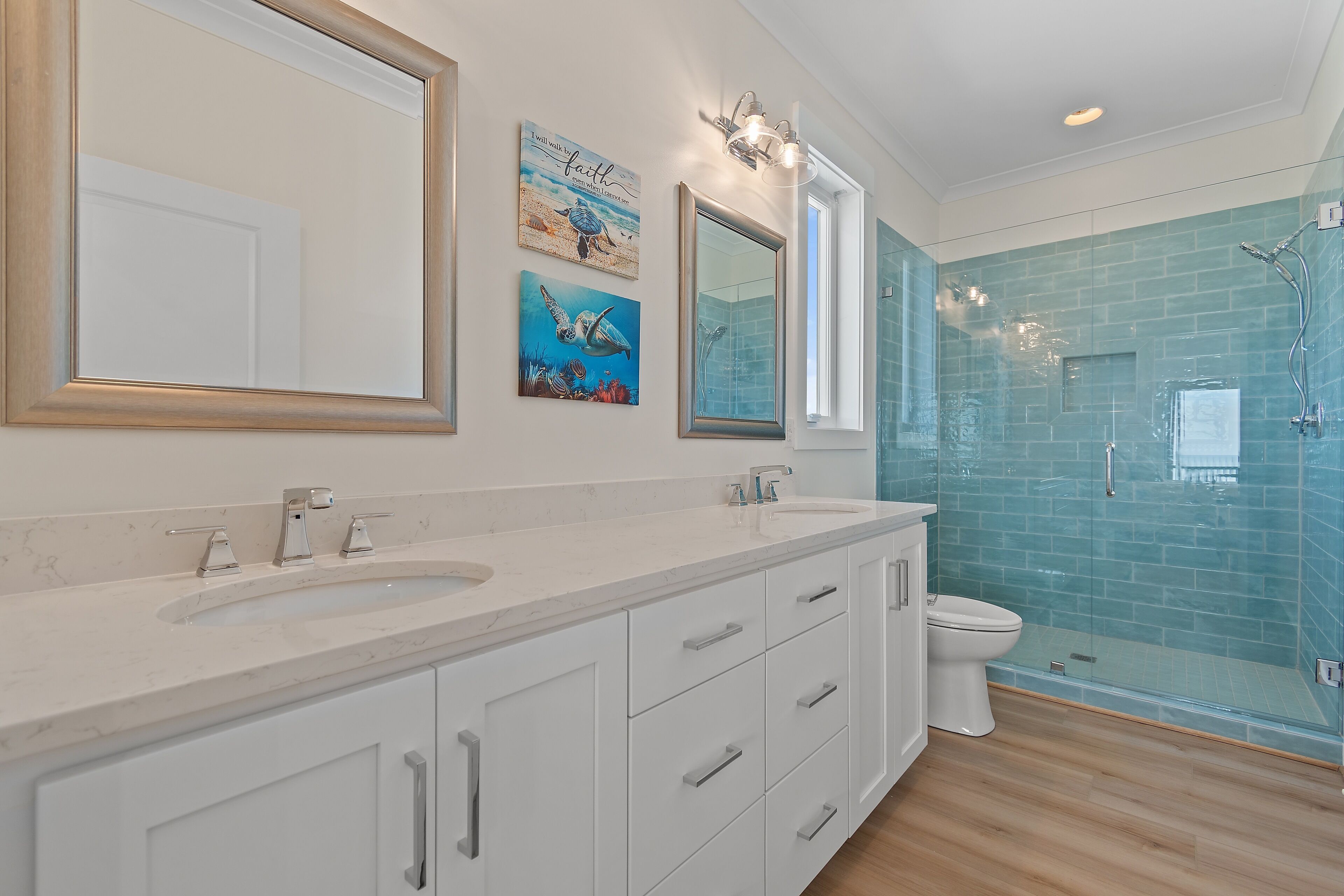 Une salle de bain avec un meuble-lavabo blanc, deux vasques, des toilettes et une douche séparée par une paroi de verre.