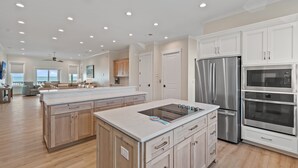 A spacious kitchen with white cabinetry, a large island, stainless steel appliances, and a view to the living area.