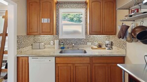A kitchen with wooden cabinets, a tiled backsplash, a window, a sink, and a dishwasher.