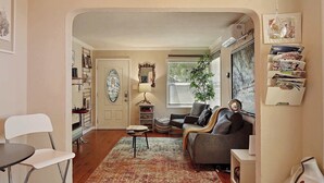 A living room with a wooden ceiling, a dining area with a white chair, and a sofa.