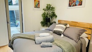 A bedroom with a bed, pillows, a bedside table, a lamp, and a potted plant.