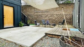 A backyard with a concrete patio, outdoor furniture, a wooden deck, and a large shade sail.