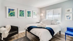 A bedroom with a bed, a black chair, a blue side table, and artwork on the wall. - Smart, Eclectic ART HOUSE near UC Davis Med Center (Sacramento)