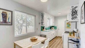 A modern kitchen with white cabinets, a green countertop, and a dining area with a wooden table and white chairs. - Smart, Eclectic ART HOUSE near UC Davis Med Center (Sacramento)