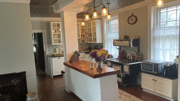 A kitchen with a central island, wooden cabinets, a microwave, and a clock on the wall. - 19th Century Mansion/Farm House (Taneytown)