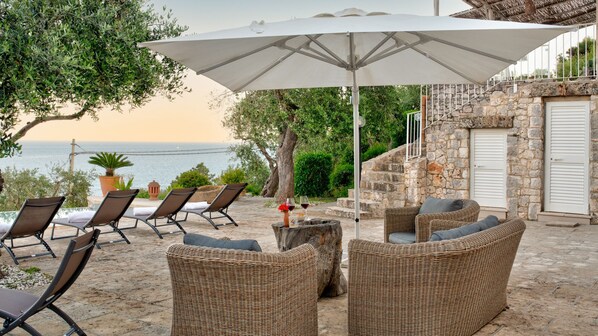 A terrace with wicker furniture, a large umbrella, and a view of the sea.