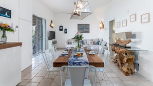 A modern dining area with a wooden table, white chairs, and a central vase with flowers. - Villa Soleluna 7+1, Emma Villas (Marina di Marittima)