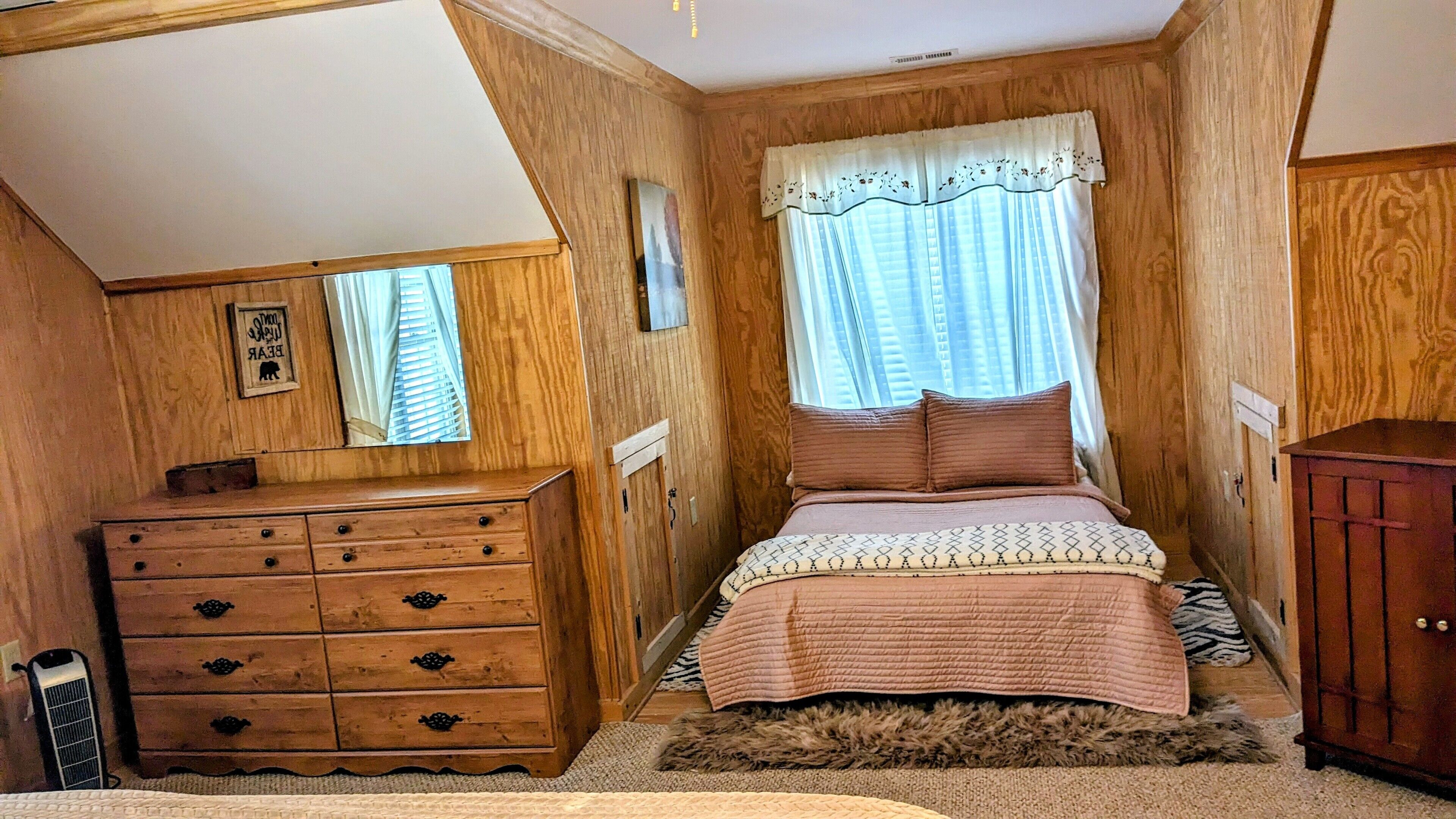 Une chambre avec une armoire en bois, un lit recouvert d’une couvre-lit à motifs, un tapis moelleux et une fenêtre avec des rideaux.