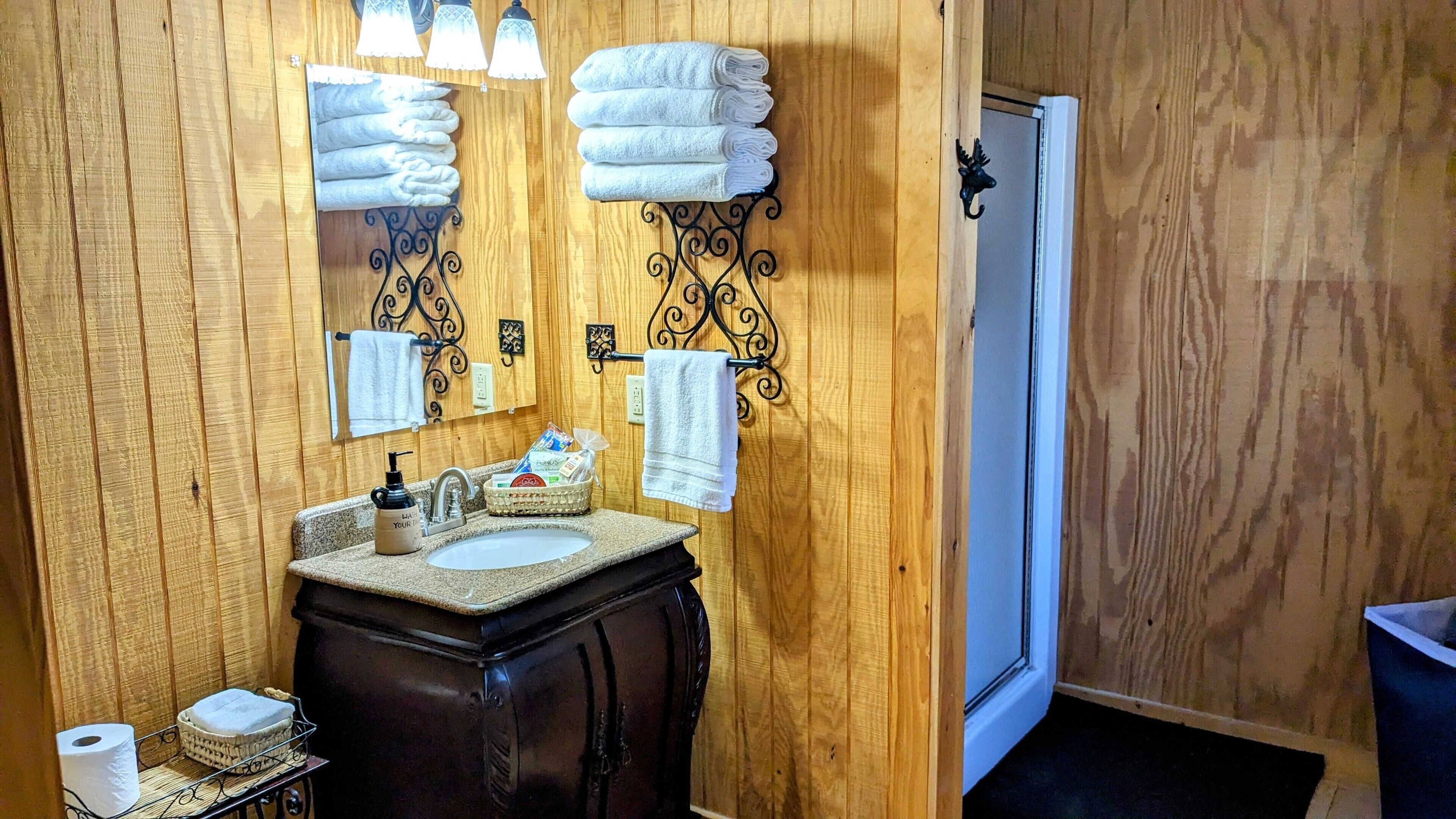 Un baño con paneles de madera, un tocador con lavabo, un espejo y dos toalleros.