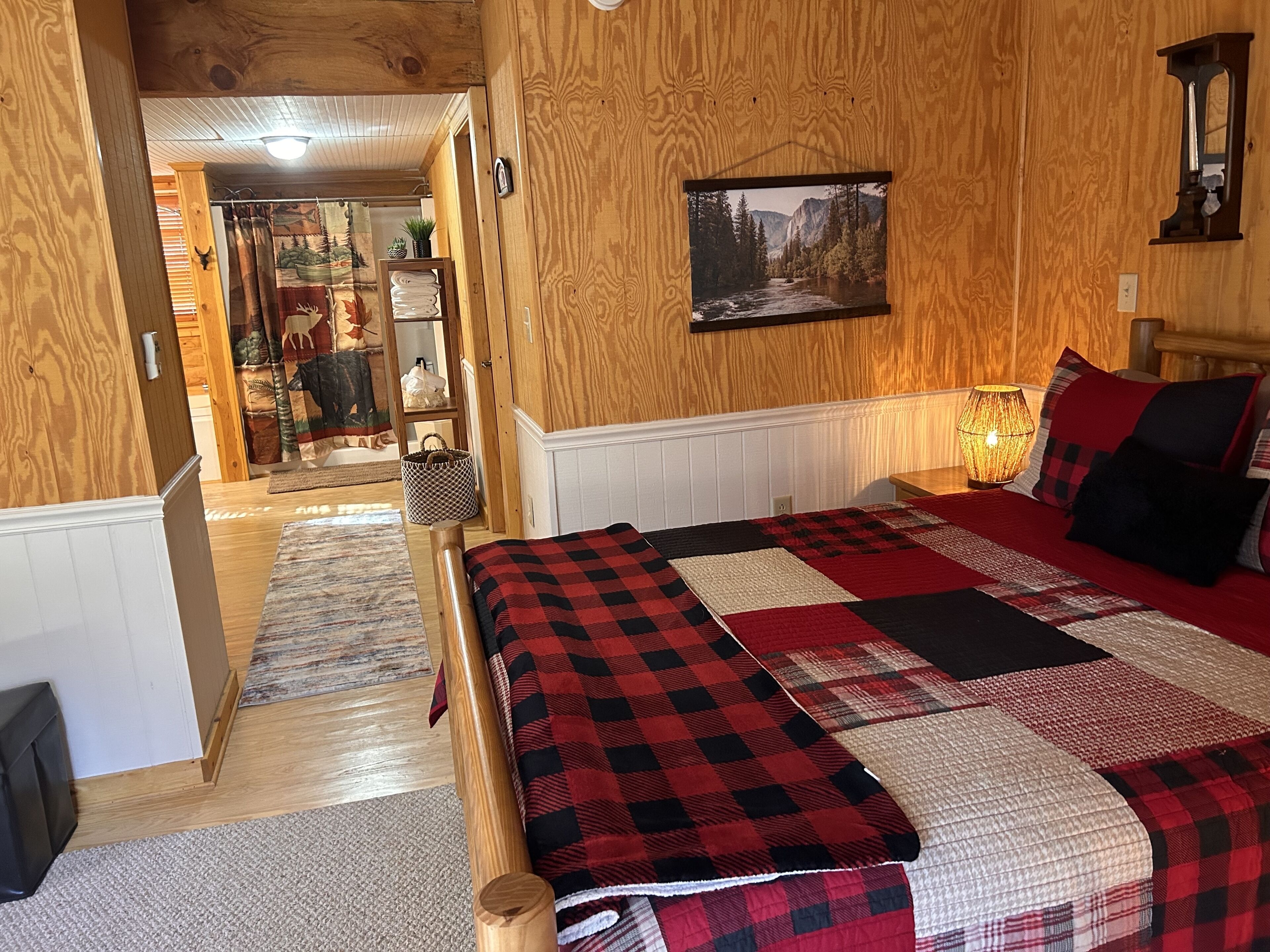 Habitación con detalles de madera, una cama, un cuadro en la pared y un pasillo que conduce a otra habitación.