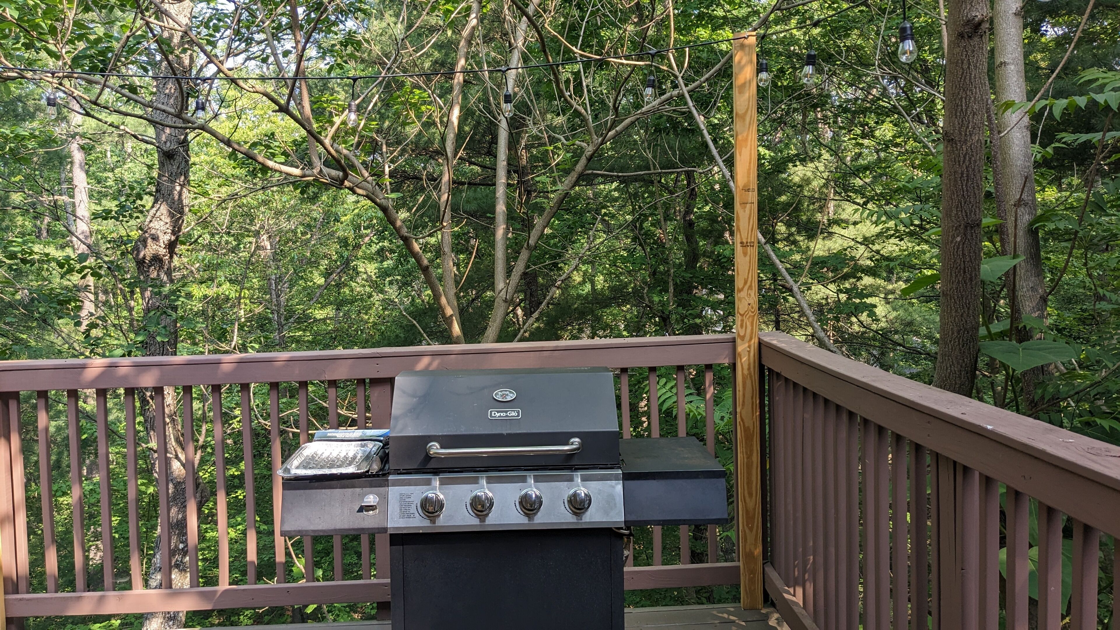 An outdoor grill on a wooden deck with a forest backdrop.