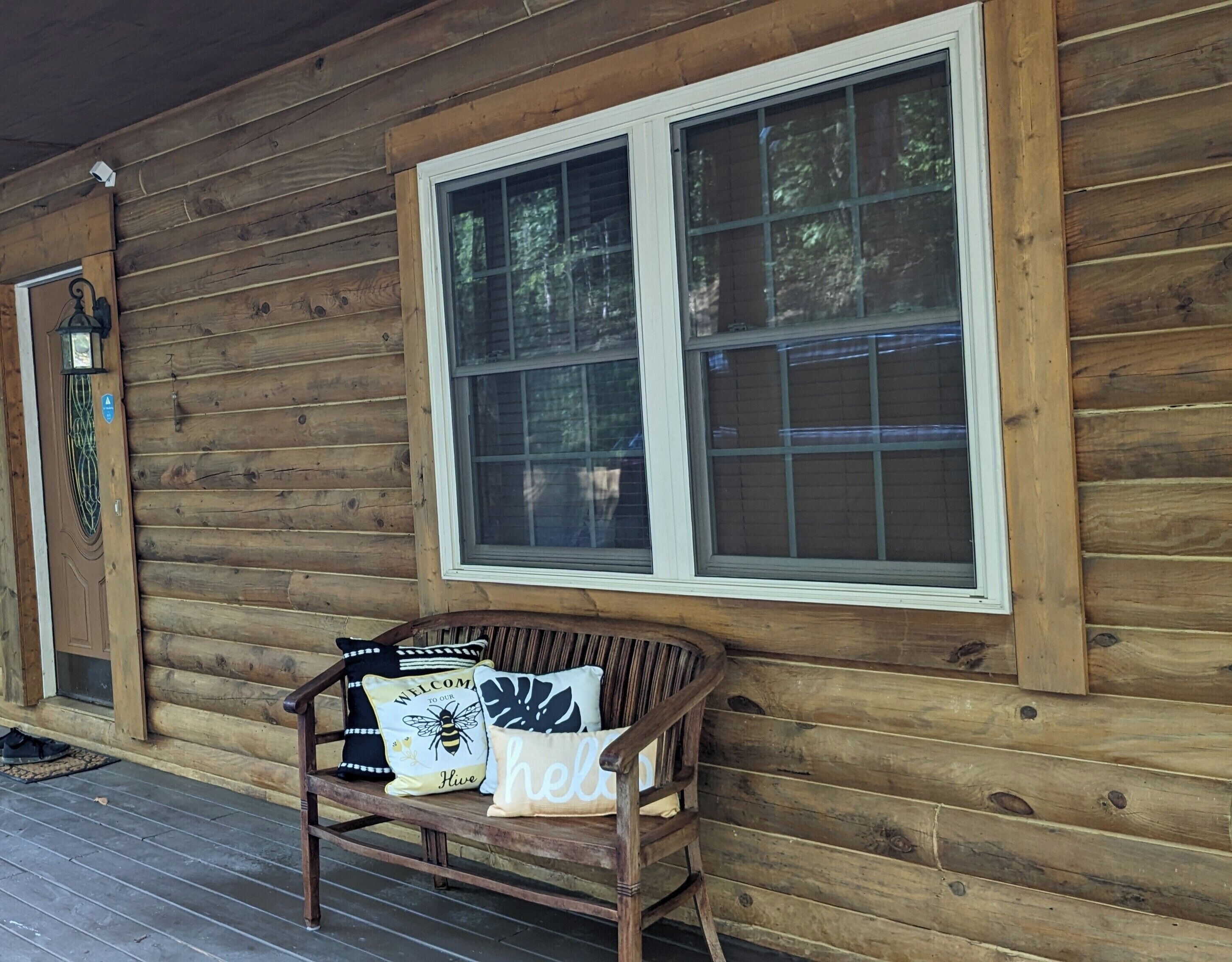A wooden cabin with a porch, a bench with cushions, and a large window.