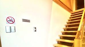 Una escalera de madera con barandilla, un letrero de prohibido fumar y un letrero de precaución en la pared.