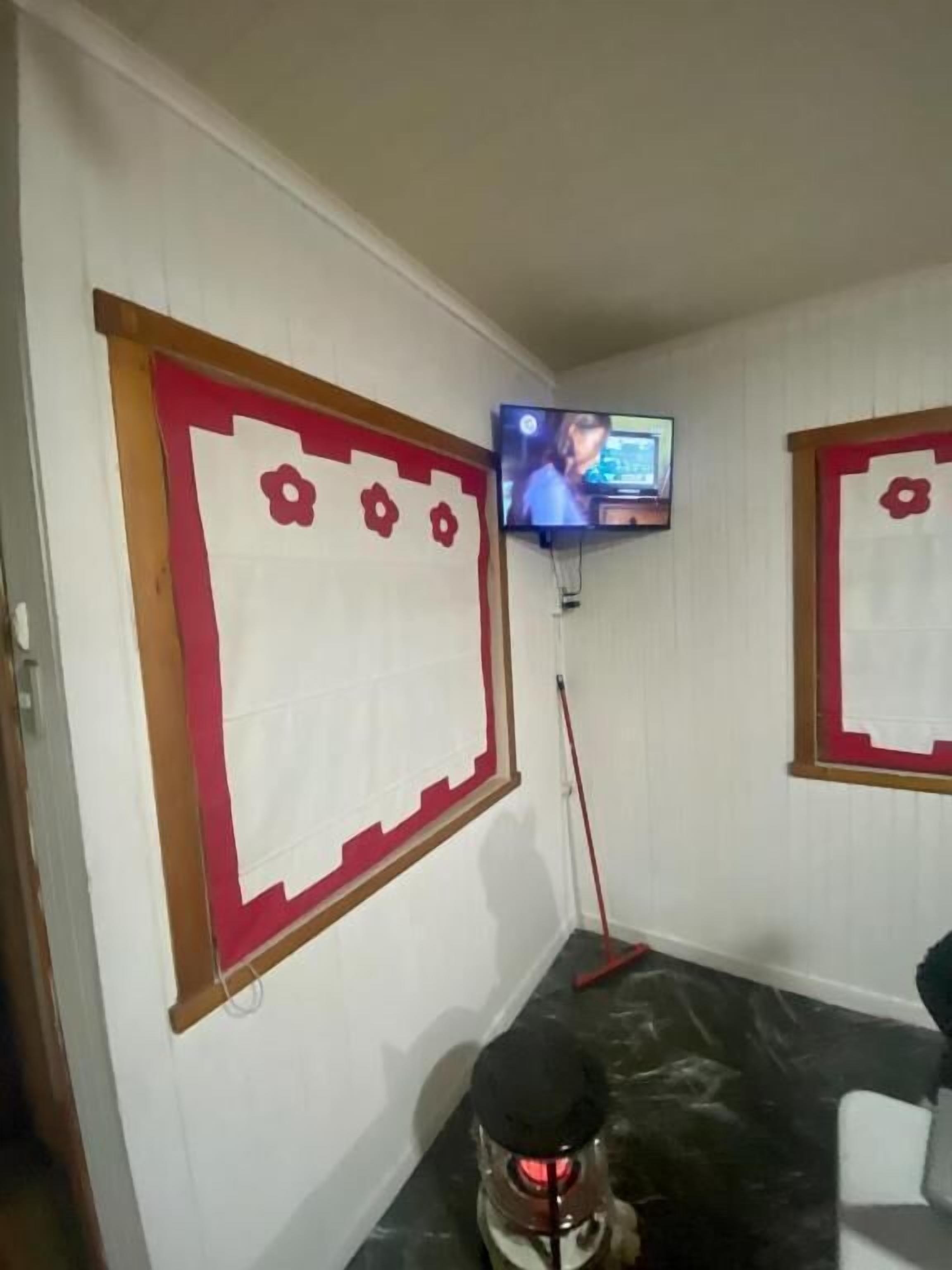 Ett rum med en tv som är monterad på väggen, en röd och vit dekorativ panel och ett svart föremål på golvet.