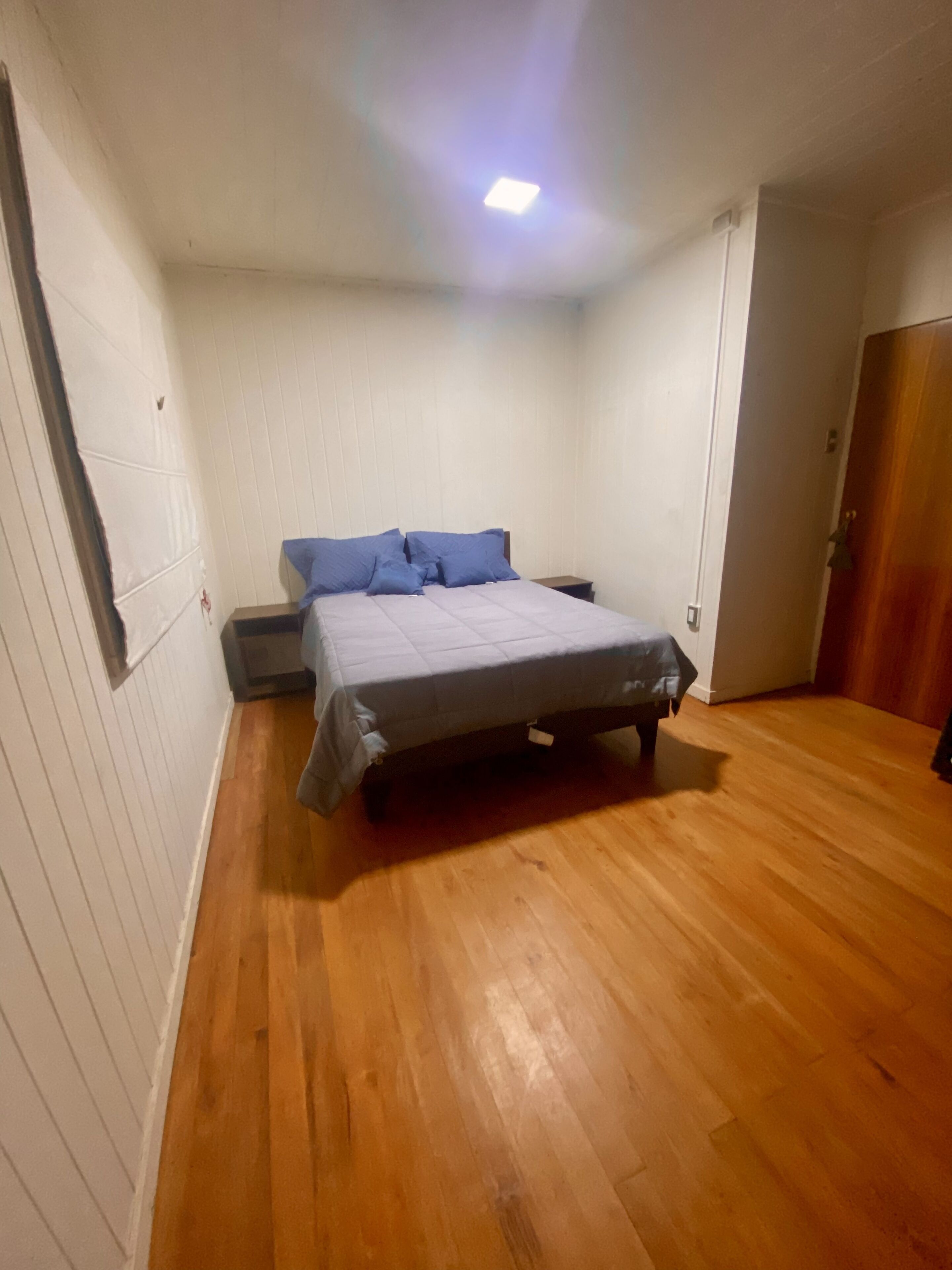 Un dormitorio con cama, piso de madera, paredes blancas y una puerta.