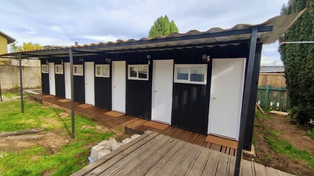 Una hilera de pequeñas cabañas de una sola habitación, con puertas y ventanas individuales, conectadas por un paseo techado.