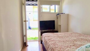 Un dormitorio con cama, televisor y armario. Hay una puerta que da a un espacio exterior.