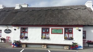 Un bâtiment traditionnel, de couleur blanche, avec un toit de chaume, une enseigne Guinness et des jardinières remplies de fleurs.
