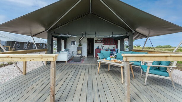 Un espace extérieur abrité, doté d’une terrasse en bois, d’un canapé et d’une table.