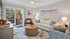 A living room with a sofa, armchair, and ottoman, a dining area with a table and chairs, and a ceiling fan.