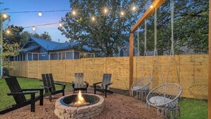 Ein Garten mit Feuerstelle, Holzstühlen und Lichterketten.