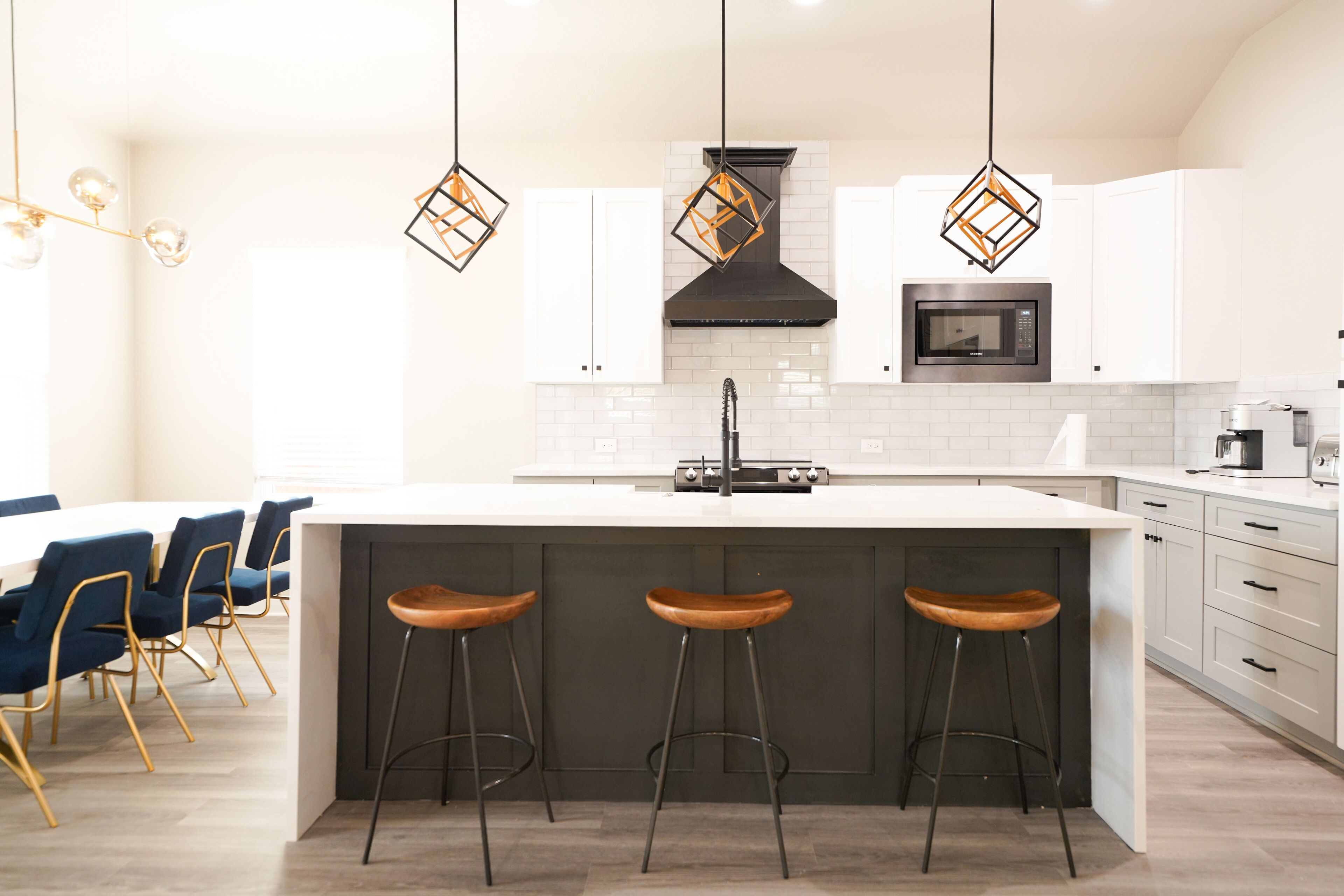 Una cocina moderna con una isla central, taburetes de bar, armarios blancos e iluminación colgante.