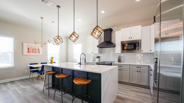 Une cuisine moderne dotée d’un îlot central, de tabourets de bar, d’appareils électroménagers en acier inoxydable et de luminaires suspendus.