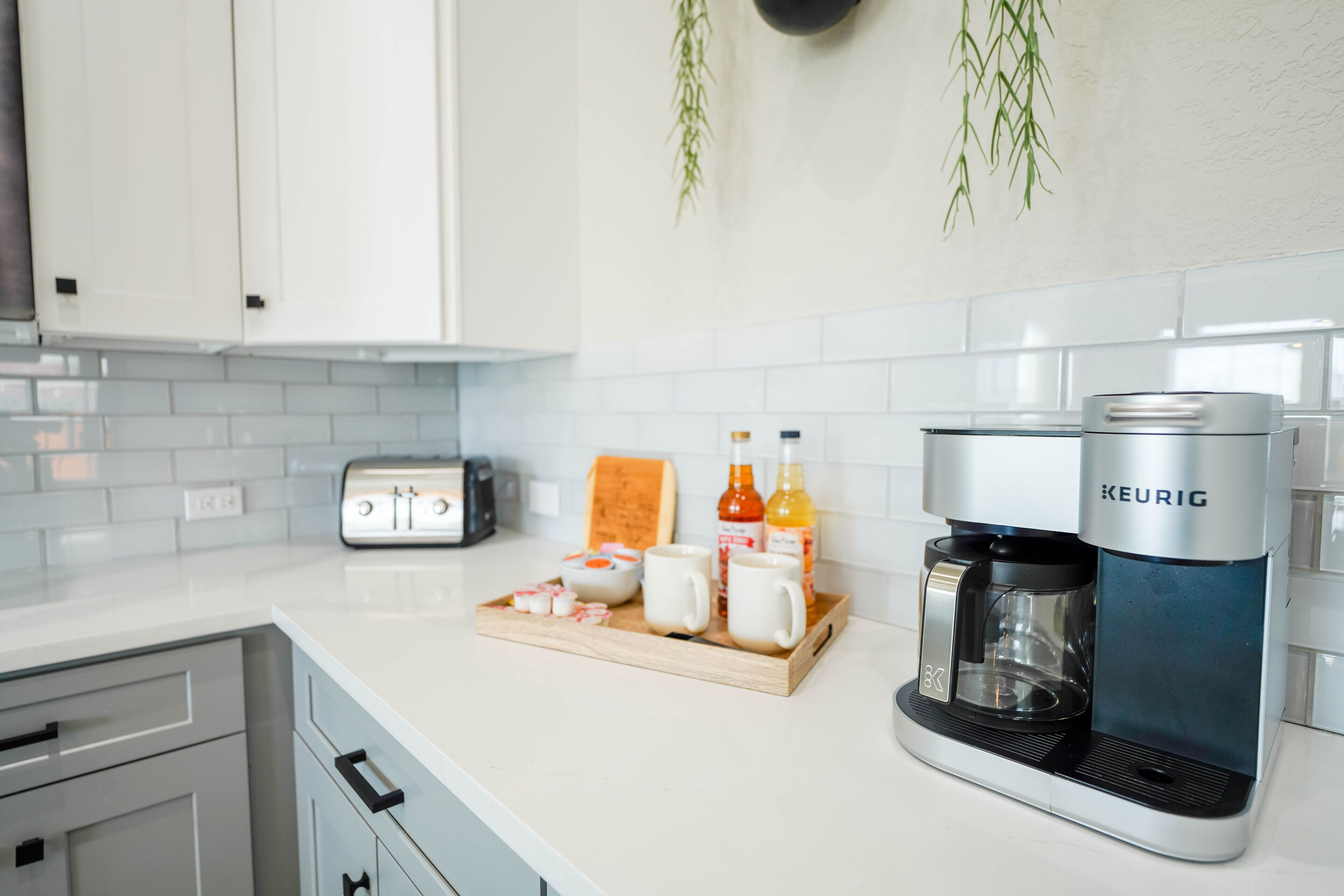 A modern kitchen with white cabinets, a coffee maker, a toaster, and a tray with cups and condiments.