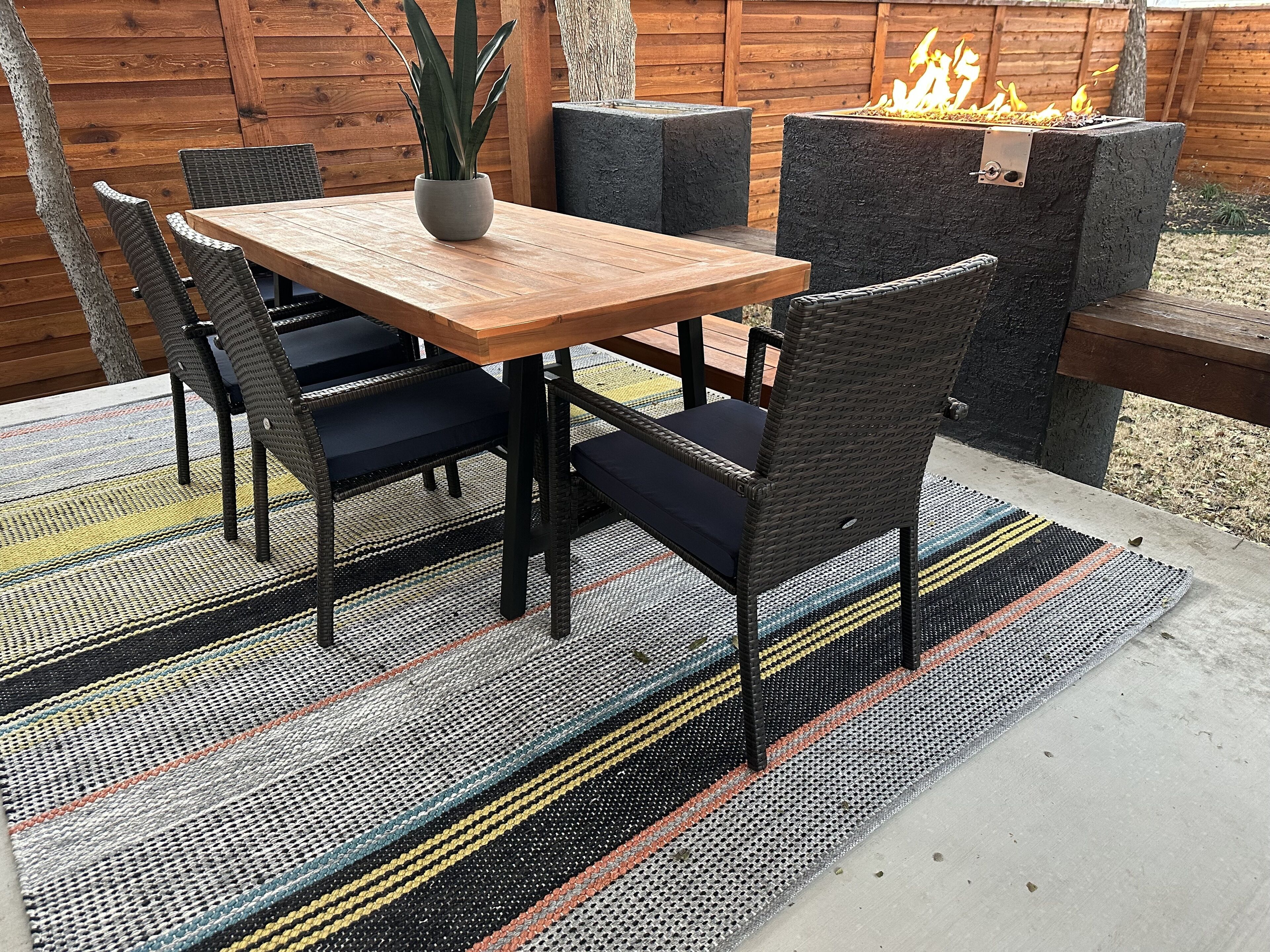 Un patio al aire libre con una mesa y sillas de madera, una planta en maceta y un brasero.