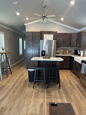 A modern kitchen with a central island, dark wooden cabinets, stainless steel appliances, and a ceiling fan. - Country Cottage with a Lake View- First Monday Nearby (Edgewood)