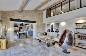 A spacious living area with a high ceiling, stone walls, a modern sofa, a unique metallic chair, and a bookshelf. - Luxurious 5* stone farmhouse (Cucuron)