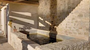 Discover a historic water well, featuring a traditional design with water flowing from the top, surrounded by a simple wall and lush greenery.
