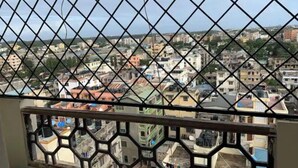 Blick durch ein Fenster mit einem diamantförmigen Gitter, das eine dicht bebautes Stadtgebiet mit verschiedenen Gebäuden und Dächern zeigt.